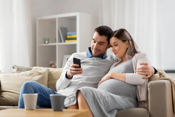 Mężczyzna i żona w ciąży z smartphone w domu — Zdjęcie stockowe