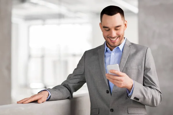 Uomo d'affari sorridente con smarphone in ufficio — Foto Stock