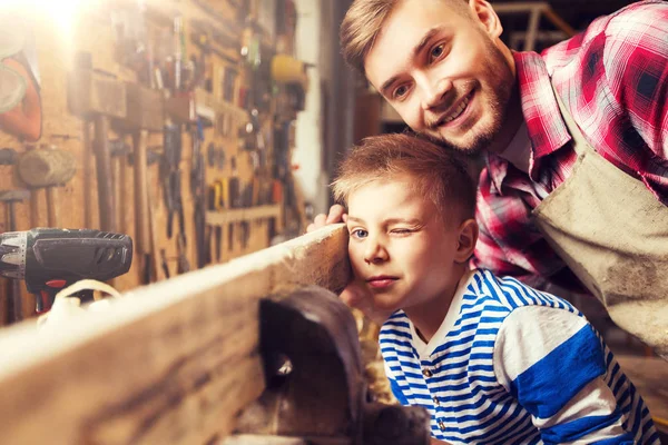 Отец и маленький сын с деревянной доской в мастерской — стоковое фото
