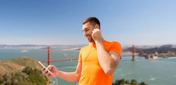 Man with smartphone and earphones over golden gate — Stock Photo, Image
