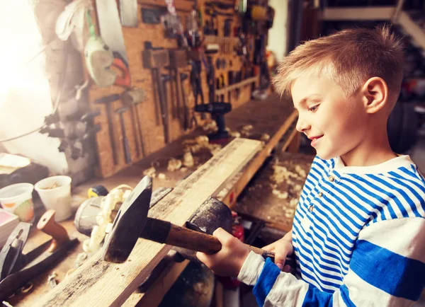 Glücklicher kleiner Junge mit Hammer und Planke in Werkstatt — Stockfoto