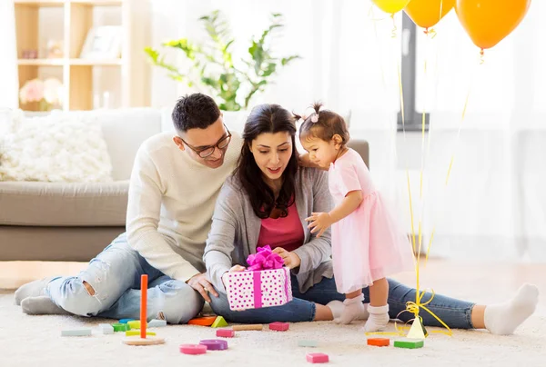 Baby-Mädchen mit Geburtstagsgeschenk und Eltern zu Hause — Stockfoto