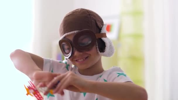 Мальчик в пилотской шляпе играет с самолетной игрушкой дома — стоковое видео