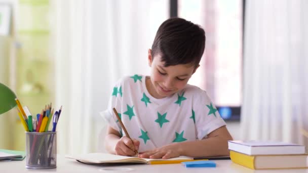 Мальчик с тетрадью и карандашами рисует дома — стоковое видео