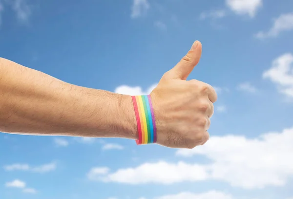带着欢乐自豪的手彩虹腕带展示大拇指 — 图库照片
