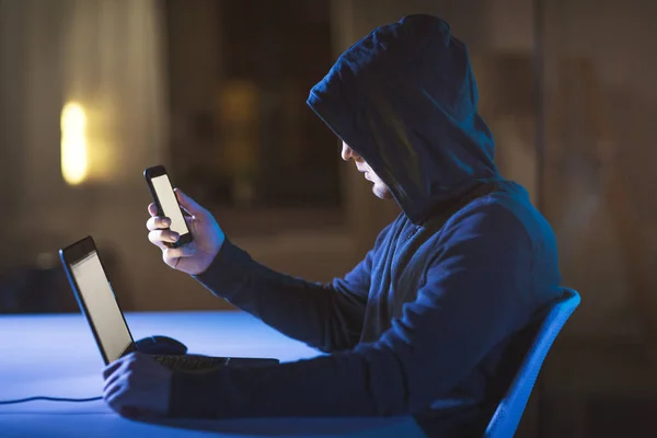 Хакер з ноутбуком і смартфоном у темній кімнаті — стокове фото