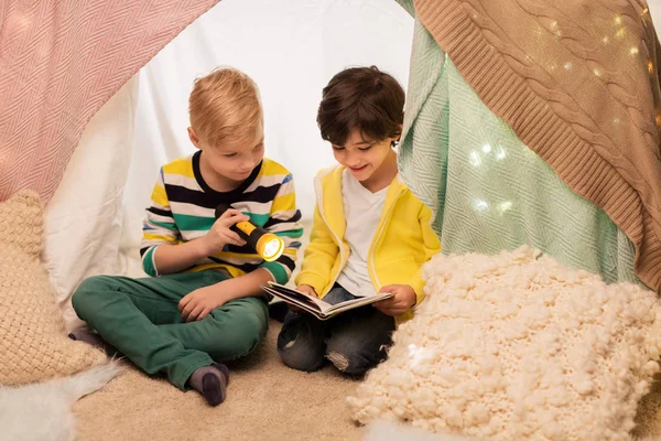 Niños felices leyendo libro en tienda de campaña de los niños en casa —  Fotos de Stock