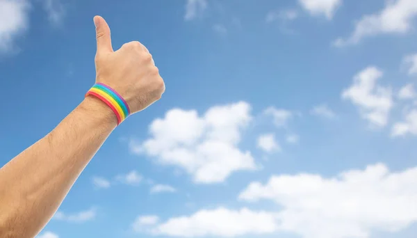 Mão com orgulho gay arco-íris pulseira mostra polegar — Fotografia de Stock