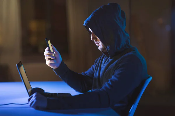 Хакер з ноутбуком і смартфоном у темній кімнаті — стокове фото