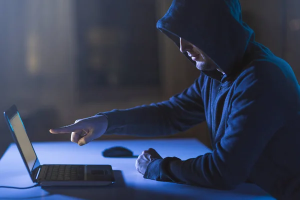 Хакер указывает на ноутбук в темной комнате — стоковое фото