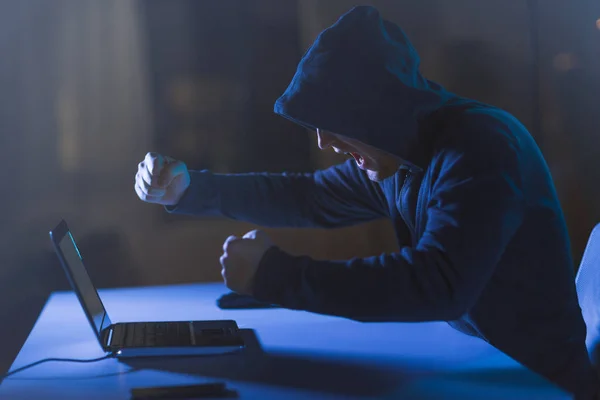 Злобный хакер с ноутбуком, кричащий в темной комнате — стоковое фото