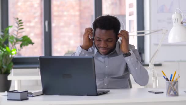 Homem de negócios com fones de ouvido e laptop no escritório — Vídeo de Stock