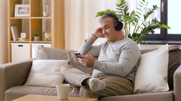 Hombre con smartphone y auriculares en casa — Vídeos de Stock