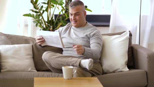 Мужчина читает газету и пьет кофе дома — стоковое видео