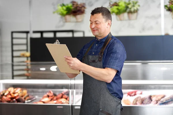 Seller at fish shop writing to clipboard — Stock Photo, Image