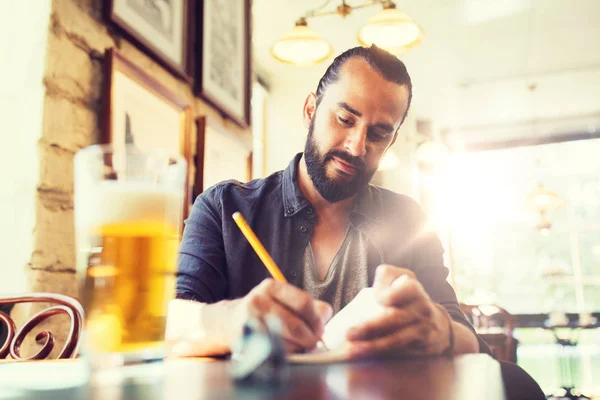 Homem com cerveja escrevendo para notebook no bar ou pub — Fotografia de Stock