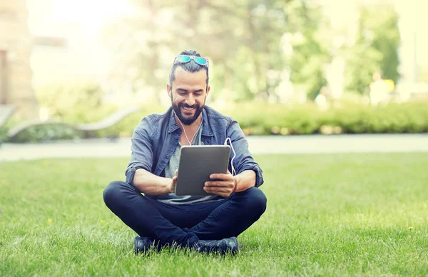 Mannen med hörlurar och TabletPC sitter på gräset — Stockfoto