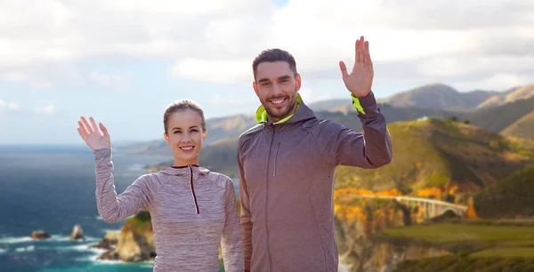 Uśmiechający się para w sportowe ubrania macha ręką — Zdjęcie stockowe