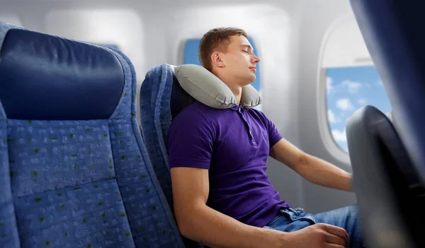 Joven durmiendo en avión con almohada de viaje — Foto de Stock