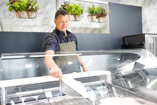 Male seller adding ice to fridge at grocery store — Stock Photo, Image