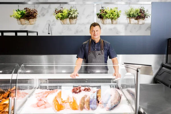 Male seller with seafood at fish shop fridge — Stock Photo, Image