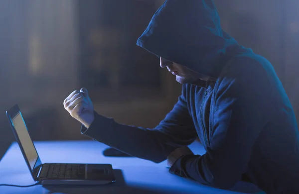 Hacker mostrando puño a portátil en habitación oscura Imagen De Stock