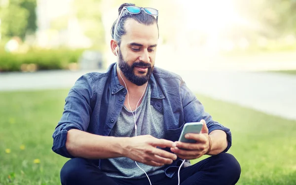 Uomo con auricolari e smartphone seduto sull'erba — Foto Stock