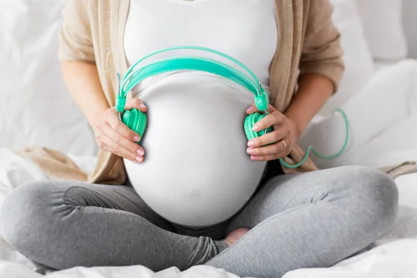 Close up de barriga de mulher grávida com fones de ouvido — Fotografia de Stock