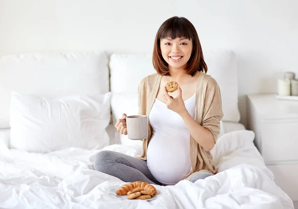 Glad gravid kvinna äta cookie i sängen hemma — Stockfoto