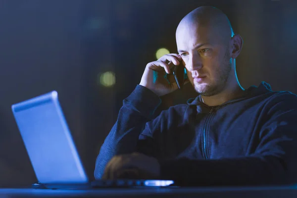 Hacker med laptop ringer på mobiltelefon — Stockfoto