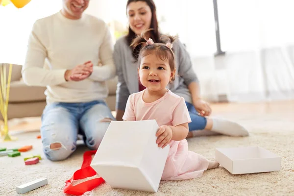 Meisje van de baby met de gift van de verjaardag en ouders thuis — Stockfoto