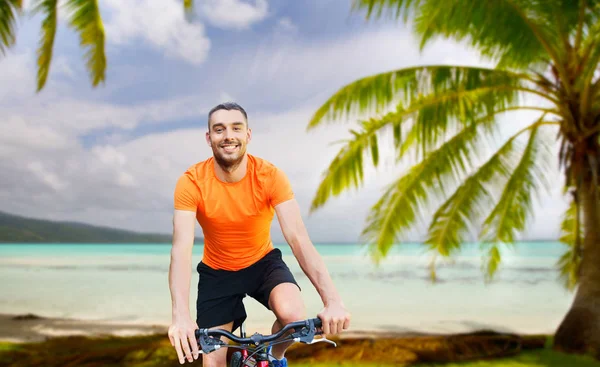 Happy young man riding bicycle over tropical beach — Stock Photo, Image