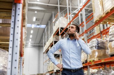 businessman calling on smartphone at warehouse clipart