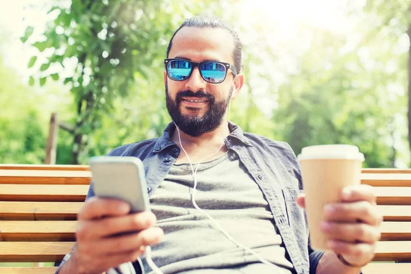 Hombre con auriculares y teléfono inteligente beber café — Foto de Stock