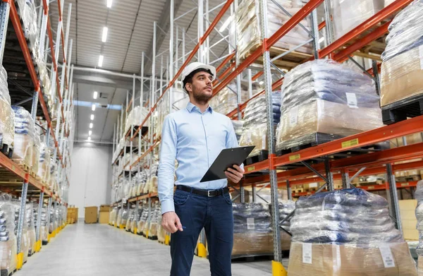 Geschäftsmann mit Helm und Klemmbrett in Lagerhalle — Stockfoto