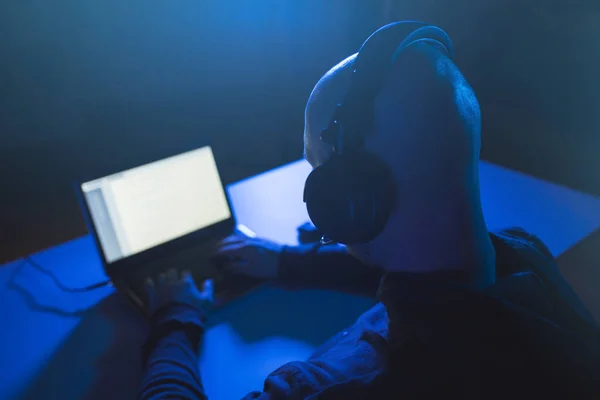 Hacker con auriculares escribiendo en el ordenador portátil en la habitación oscura — Foto de Stock