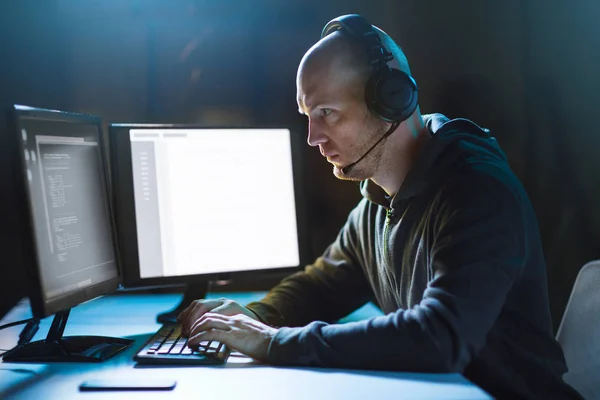 Хакер с компьютером и гарнитурой в темной комнате — стоковое фото