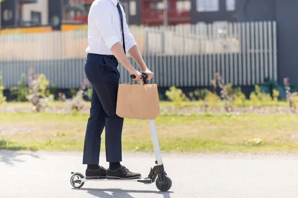 Businessman with takeaway paper bag riding scooter — Stock Photo, Image