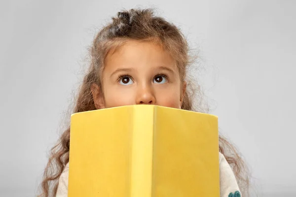 Petite fille cachée derrière livre jaune — Photo