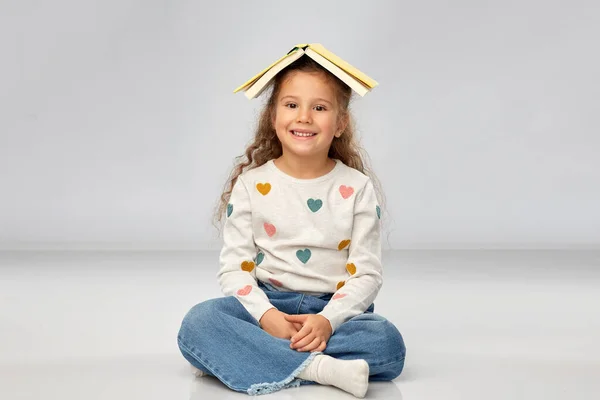 Портрет усміхненої дівчини з книгою на голові — стокове фото