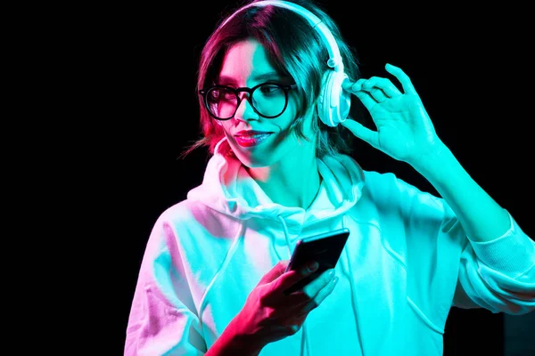 Vrouw in hoofdtelefoon met smartphone in neon verlichting — Stockfoto