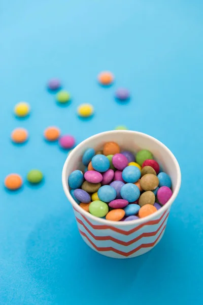 Caramelos gotas en taza de papel sobre fondo azul —  Fotos de Stock