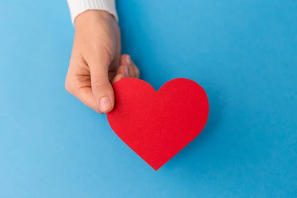 Ręka trzymając czerwony kształt serca na niebieskim tle — Zdjęcie stockowe