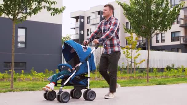 Otec s dítětem v kočárku pěšky po městě — Stock video
