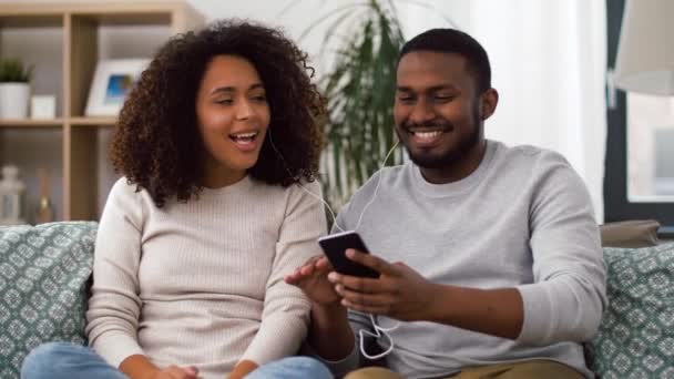 Ευτυχισμένο ζευγάρι με smartphone και ακουστικά στο σπίτι — Αρχείο Βίντεο