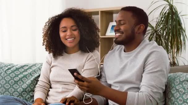 Feliz pareja con smartphone y auriculares en casa — Vídeos de Stock