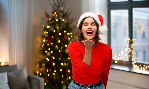 Žena v santa klobouk posílání vzduchu polibek na Vánoce — Stock fotografie
