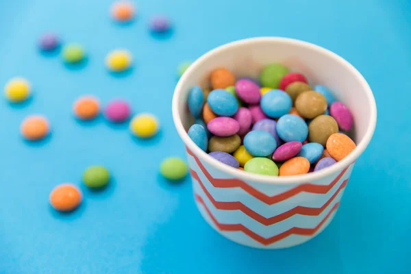 Caramelos gotas en taza de papel sobre fondo azul —  Fotos de Stock