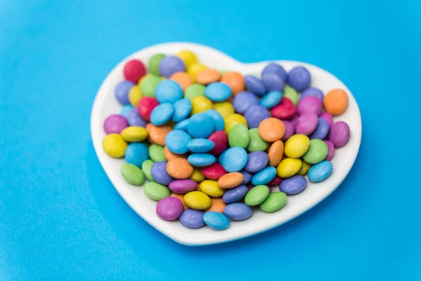 Bonbons auf herzförmigem Teller vor blauem Hintergrund — Stockfoto