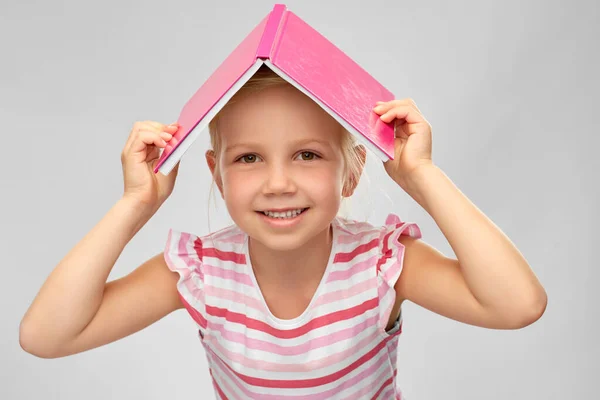 Kleines Mädchen mit Bücherdach auf dem Kopf — Stockfoto